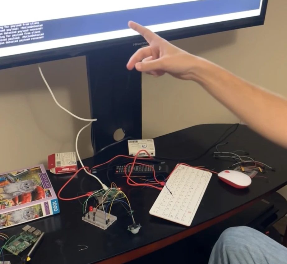 A Raspberry Pi wired to a breadboard with a red LED and a motion sensor, with the program output on a screen behind it